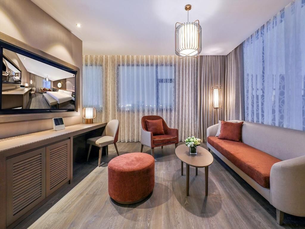 Ein modernes Hotelzimmer mit einem Bett, einem Schreibtisch, einer Couch, einem runden Hocker und einem großen Spiegel.