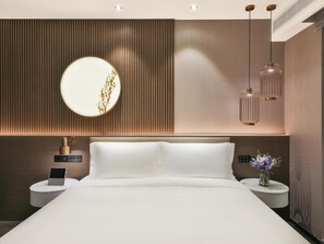 Quarto moderno com uma cama grande, mesas de cabeceira, uma luminária fixada na parede e um espelho decorativo.