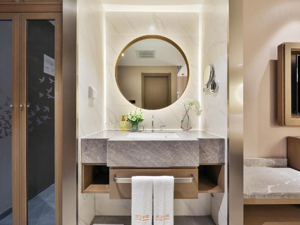 Un baño moderno con tocador de mármol, espejo redondo, toallero y una pequeña planta.