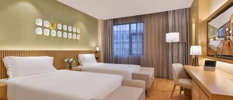 Habitación de hotel con dos camas, un escritorio y una silla. Cuenta con un ventanal con cortinas, una lámpara de pared y un adorno en la pared.