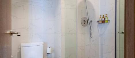 A bathroom with a toilet, a glass shower enclosure, and a shelf with toiletries.
