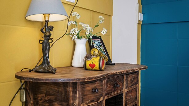 Un aparador de madera con una lámpara, un jarrón blanco con flores y un cuadro enmarcado.