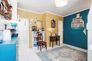 Ein Flur mit einem blauen Schrank, einem Bücherregal, einem Sessel, einem kleinen Tisch mit einer Lampe und einer Wand mit gerahmten Bildern.