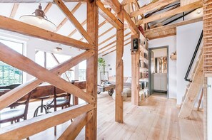 Ein geräumiger Raum mit freiliegenden Holzbalken, einem Essbereich mit Stühlen und einem Tisch sowie einer Treppe.