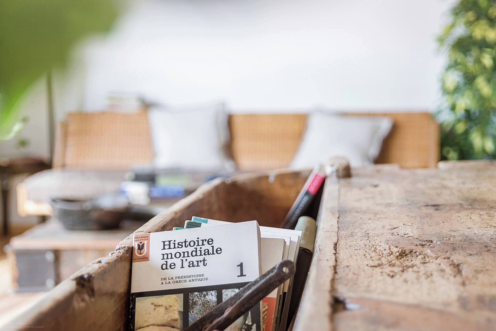 Eine Holzbank mit Büchern, einem Stift, einem Kissen und einem kleinen Tisch mit einer Schüssel im Hintergrund.