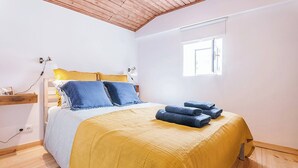 Une chambre à coucher avec un lit, une table de chevet, une lampe, une fenêtre et une prise électrique au mur.