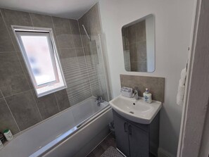 A bathroom with a bathtub, a sink, a mirror, and a window. - Cozy House in Liverpool (Kensington)