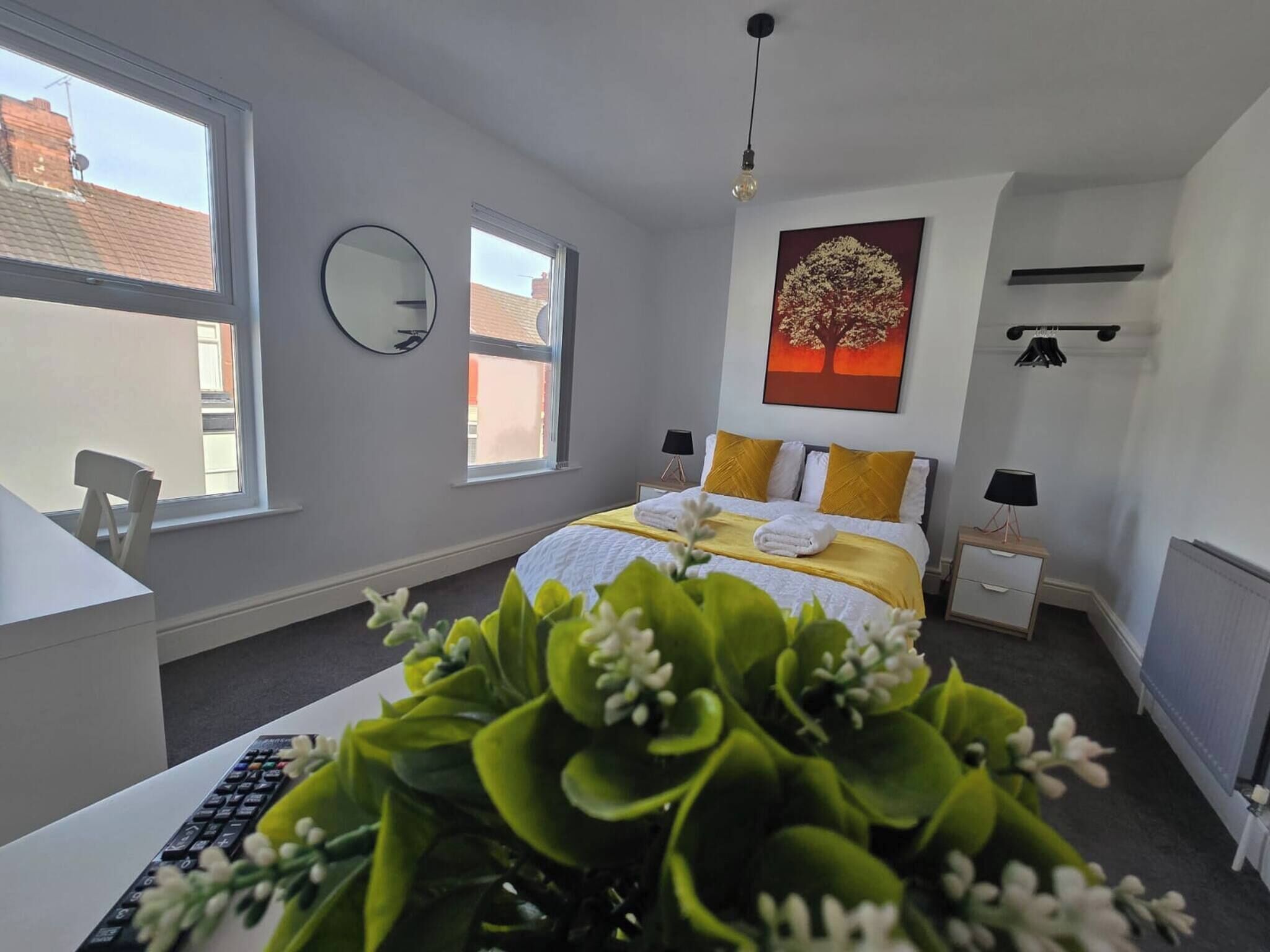 Ein modernes Schlafzimmer mit einem Bett, Nachttischen, einem Schreibtisch, einem Spiegel und einem großen Fenster.