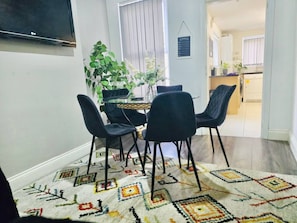 Ein Essbereich mit Tisch, Stühlen, einem Blumentopf und einem gemusterten Teppich.