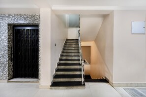 Una escalera con barandilla que lleva a un rellano con interruptor de luz y una puerta.