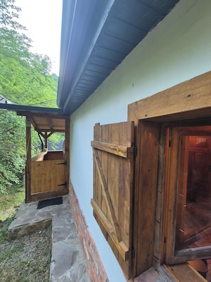 Fachada de madera con base de piedra, una puerta de madera y una ventana con persiana de madera.