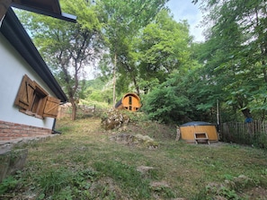 A rustic cabin with a wooden exterior, surrounded by a natural landscape with trees and a small wooden structure.