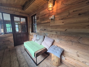 Interior de una cabaña de madera con una cama, un banco e iluminación en la pared.