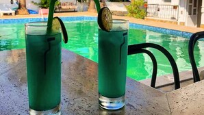 Dos vasos de bebida verde con pajitas y una rodaja de lima sobre una mesa junto a una piscina.