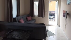 Una sala de estar con sofá, mesa, televisor y vistas al exterior.