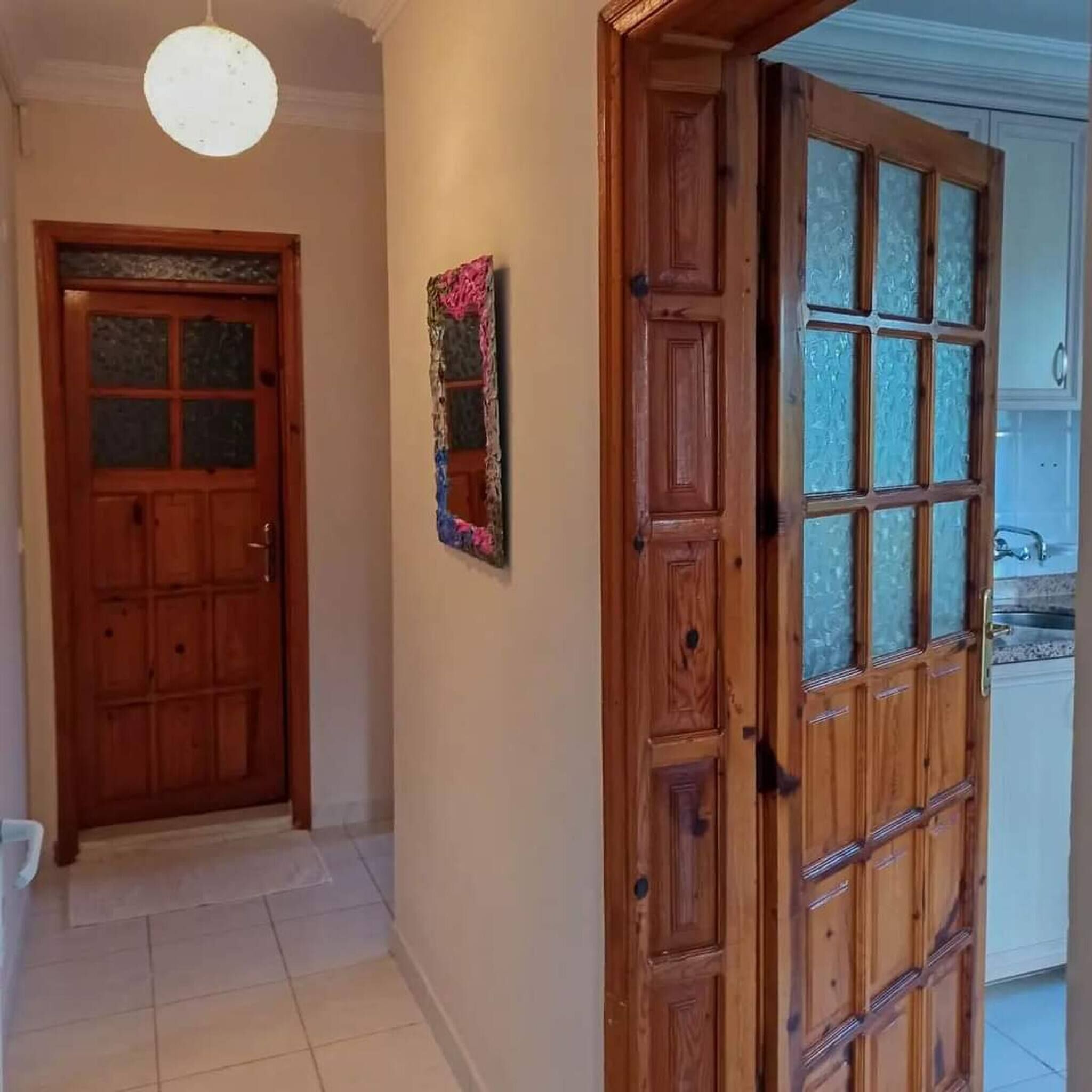 A hallway with a wooden door and a glass door, a light fixture, and a tiled floor.