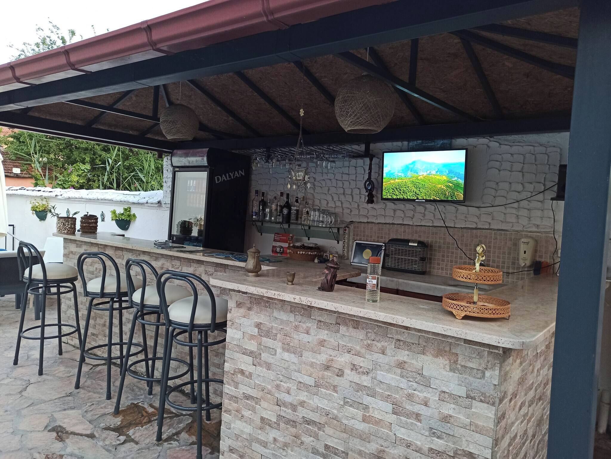 An outdoor bar area with a stone counter, bar stools, a television mounted on a stone wall, and various bar accessories.