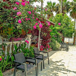 An outdoor seating area with chairs and tables, surrounded by lush greenery and flowering plants. - Garden-view suite room (Ortaca)