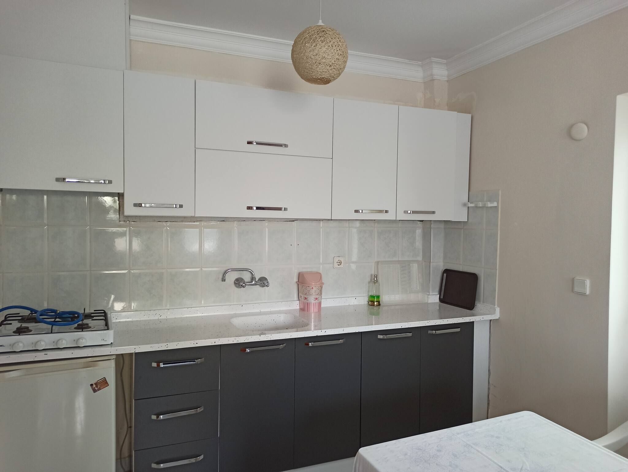 A kitchen with white cabinets, a gas stove, a sink, and a hanging light fixture.