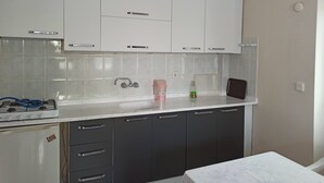 Cocina con gabinetes blancos, estufa a gas, pileta y lámpara colgante.