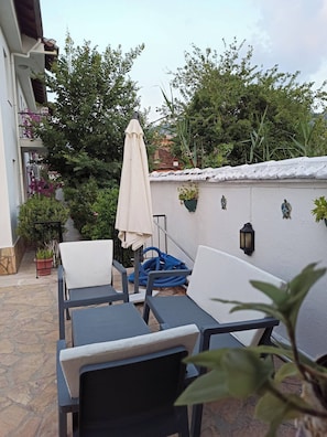 An outdoor seating area with chairs and tables, a white umbrella, and potted plants.