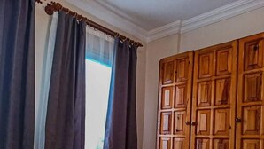 Habitación de hotel con cama, ventana con cortinas y armario de madera.