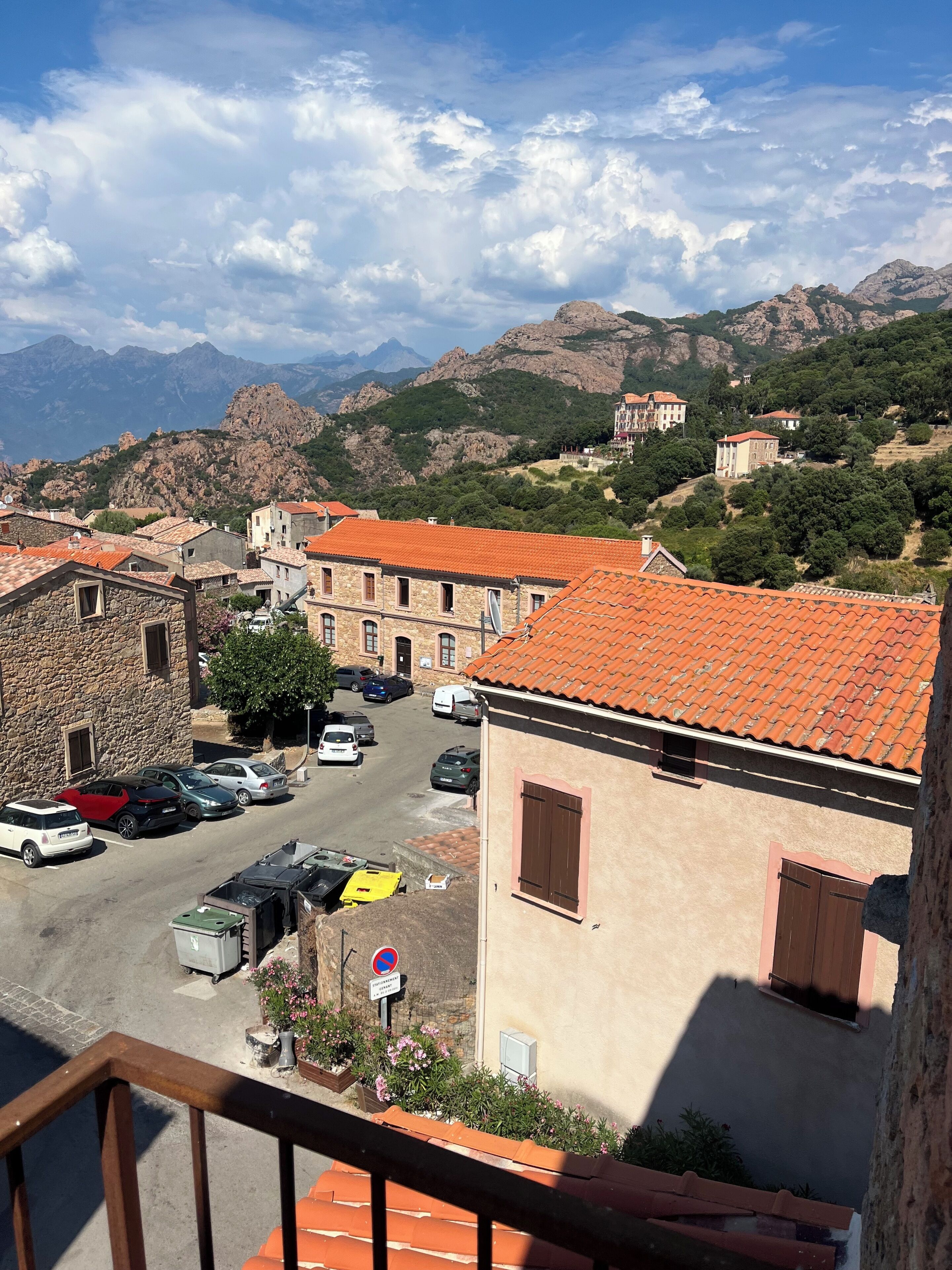Une ville avec des bâtiments en pierre, un parking et des montagnes en arrière-plan.