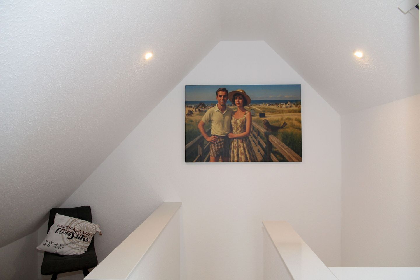 A painting of a couple on a beach, a white wall, and a small black chair with a pillow.