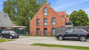 A modern brick building with a sloped roof, a driveway, and two cars parked in front. - Lüttje Sünn - Lüttje Sünn - Your oasis of well-being in Norddeich (Norden)