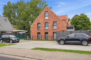 Ein modernes Backsteinhaus mit geneigtem Dach, einer Auffahrt und zwei geparkten Autos davor.