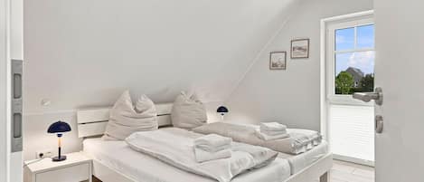 Een moderne slaapkamer met een schuine kap, een bed met witte lakens, twee nachtkastjes met lampen en een raam met uitzicht.