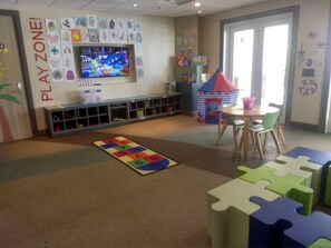 A play area with a play zone sign, a television, a play mat, a puzzle table, and a bookshelf. - Disney Dreams Luxury Home with Private Water Park (Kissimmee)