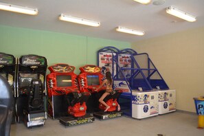 Arcade machines, a blue play structure, and a basketball-themed storage unit in a room with green walls and fluorescent lighting. - Disney Dreams Luxury Home with Private Water Park (Kissimmee)