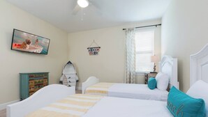 A bedroom with two beds, a ceiling fan, a television, a beach-themed sign, and a window with curtains. - Disney Dreams Luxury Home with Private Water Park (Kissimmee)