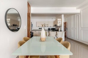 Eine moderne Küche mit weißen Schränken, einem Esstisch mit Stühlen und einem großen Spiegel an der Wand.