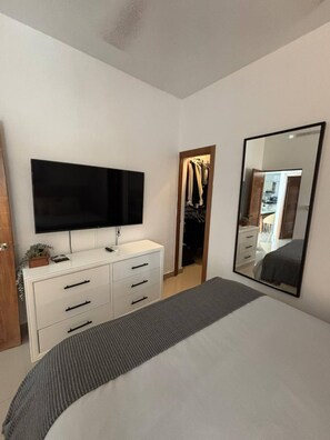 Ein Schlafzimmer mit einem Bett, einem Schminktisch, einem Fernseher, einem Spiegel und einem Kleiderschrank.