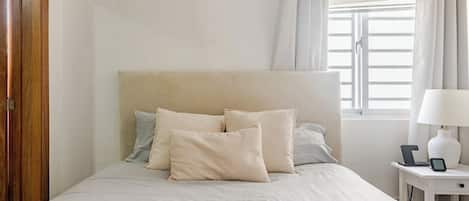 Una cama con cabecera, almohadas, una mesita de noche con lámpara y teléfono.
