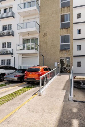 A multi-story residential building with balconies, a garage, and parked cars. - Modern 2BR Apartment Near Agora Mall (Santo Domingo)