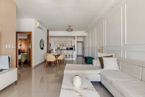 A modern living room with a sofa, a coffee table, and a dining area with chairs. - Modern 2BR Apartment Near Agora Mall (Santo Domingo)