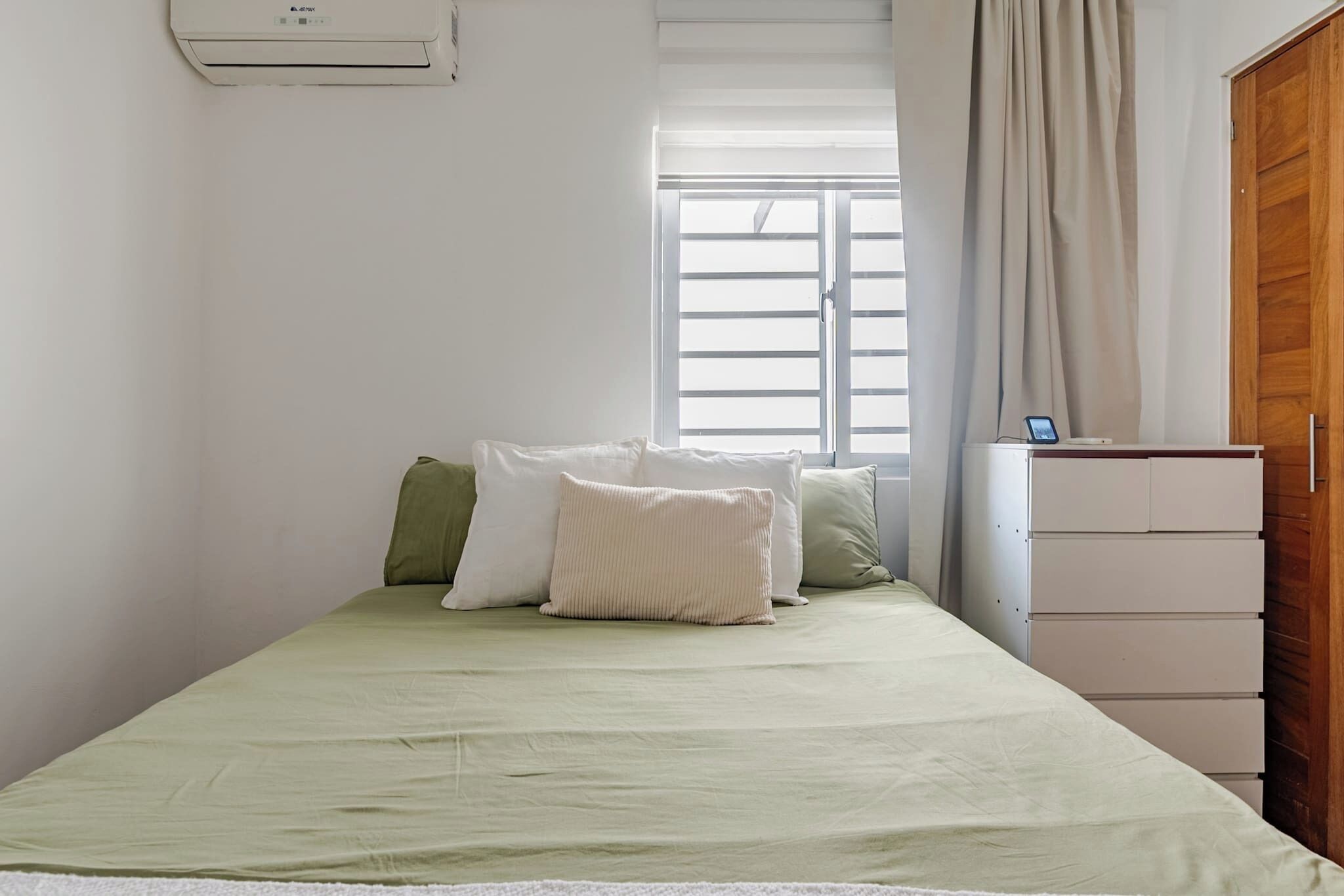 Un dormitorio con cama, ventana con persianas, armario y equipo de aire acondicionado.