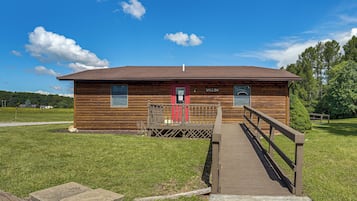 Una cabaña de madera con puerta roja, una terraza de madera y un letrero que indica un cuarto de baño.