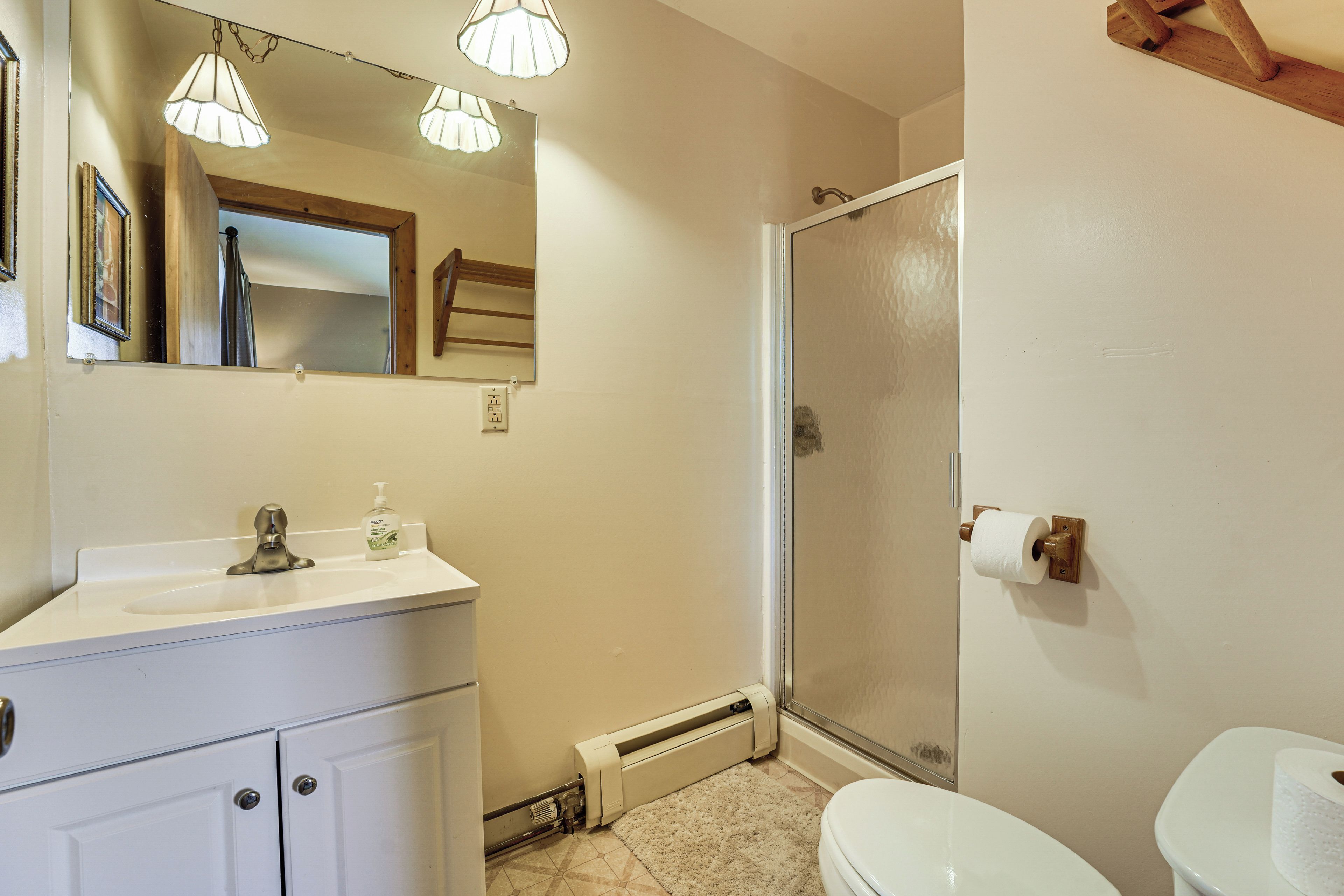A bathroom with a toilet, sink, mirror, and shower.
