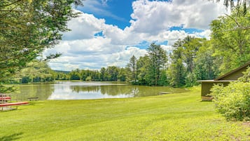 A tranquil lakeside setting with a grassy lawn, a wooden dock, and a small building, likely a cabin or guesthouse.