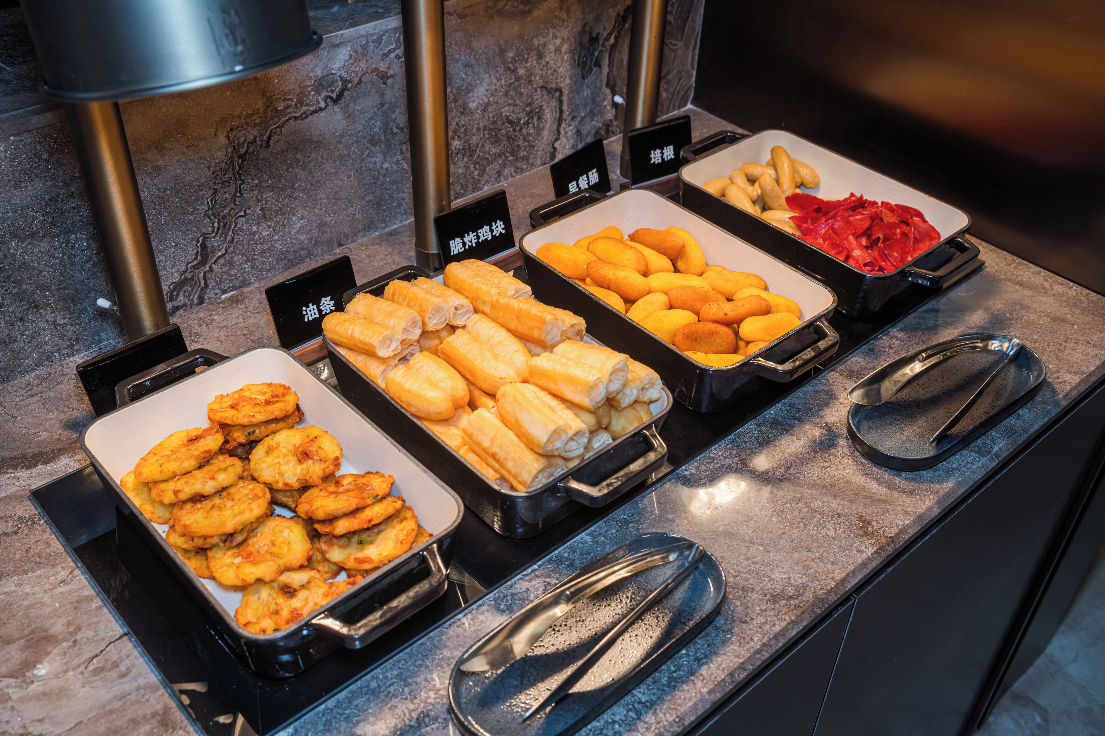Un buffet proposant une variété de plats, notamment des aliments frits, des petits pains et un plateau de viande rouge.