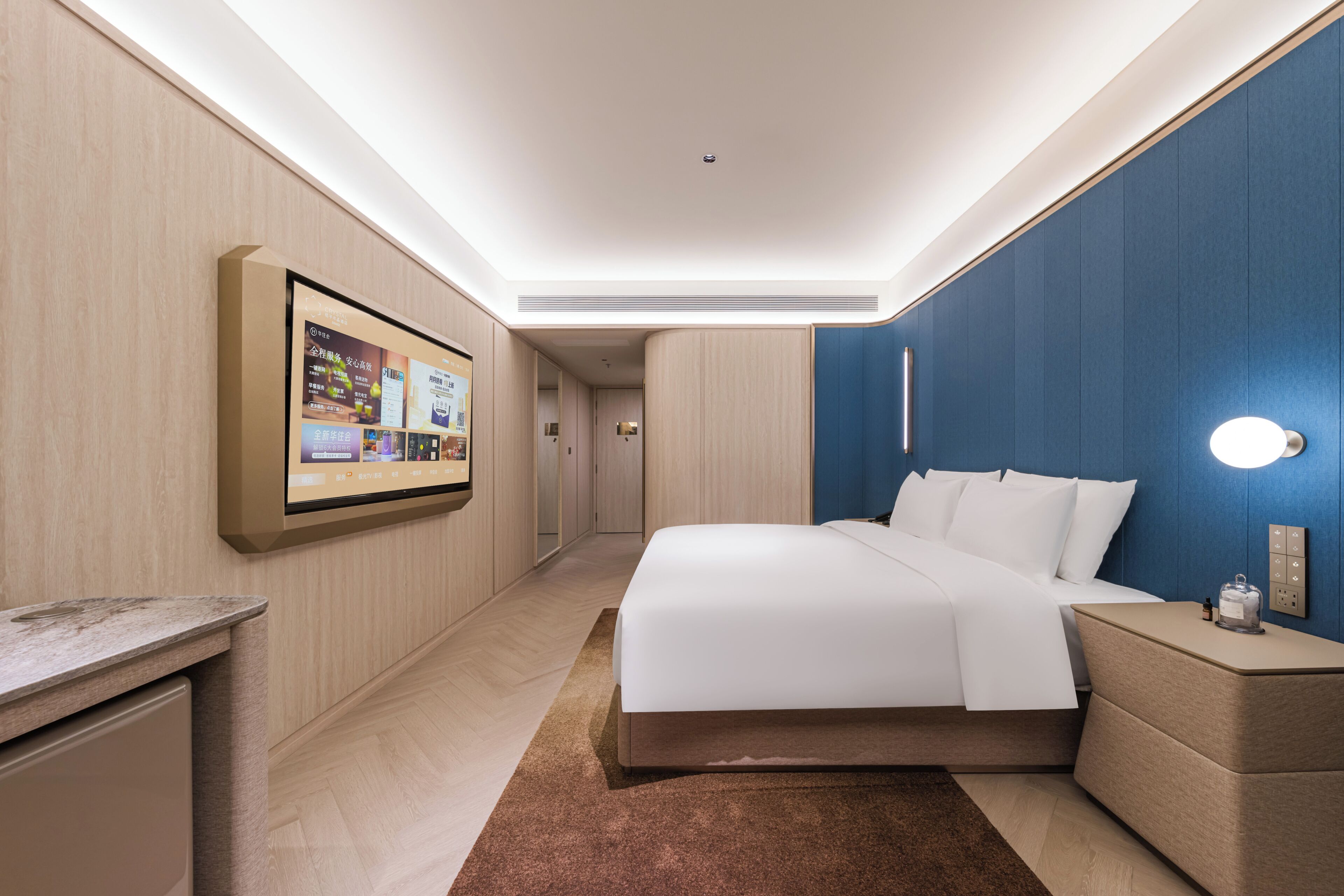 A modern hotel room with a large bed, a bedside table, a wall-mounted TV, and a ceiling light.