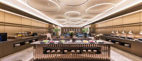 Una moderna hall d'albergo con un'area buffet centrale, un angolo salotto e una reception.