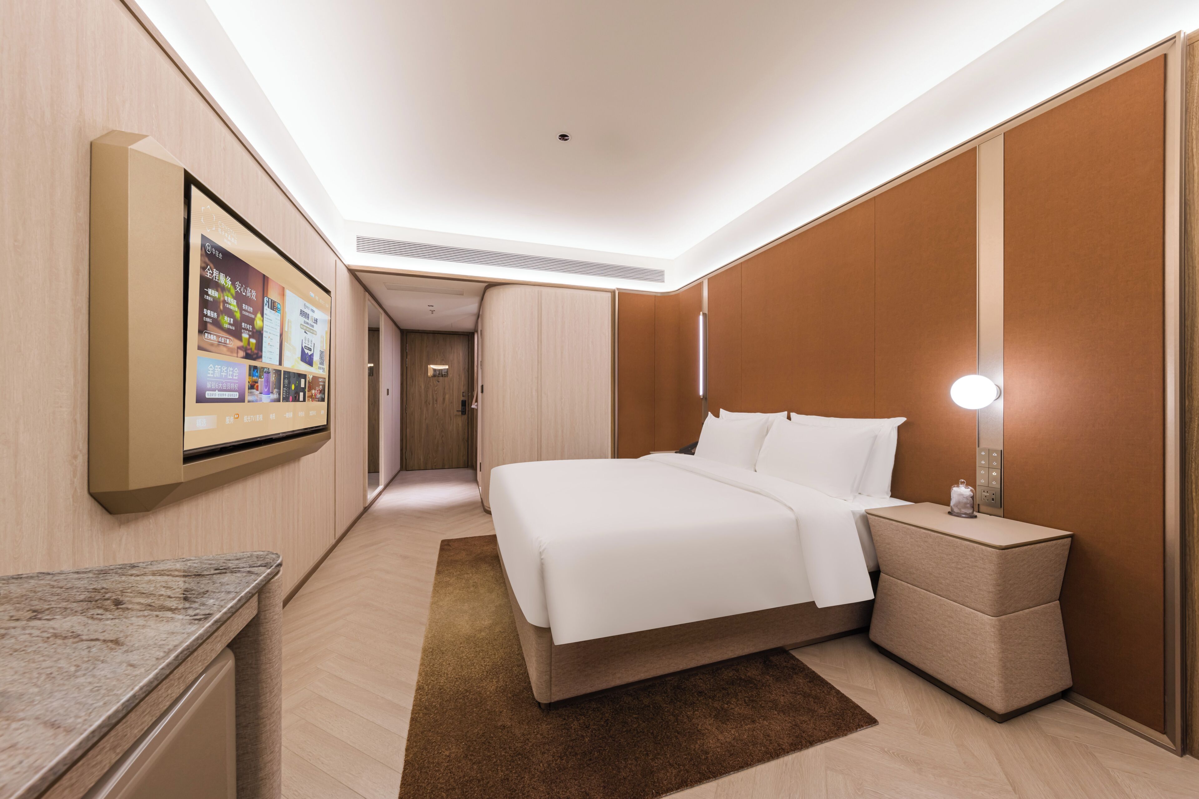 Een hotelkamer met een bed, nachtkastje, wandtelevisie en een deur naar een gang.