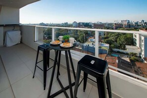A balcony with a table set for two, a chair, and a small plant. - Corporate Stays First Living - 502 (Asunción)