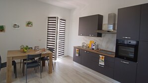 A modern kitchen with dark cabinets, a built-in oven, and a dining area with a wooden table and chairs. - Vacation Home 300 m from the Sea, Ideal for Those Seeking Relaxation, Privacy, and Comfort (Avola)