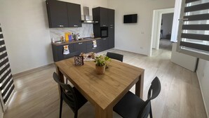 A modern kitchen with dark cabinets, a wooden dining table, and a TV mounted on the wall. - Vacation Home 300 m from the Sea, Ideal for Those Seeking Relaxation, Privacy, and Comfort (Avola)